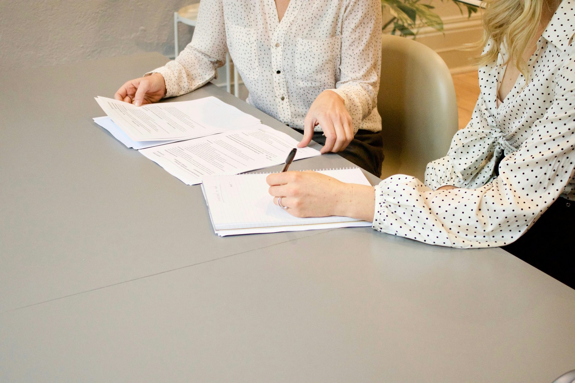 woman signing on white printer paper beside woman about to touch the documents